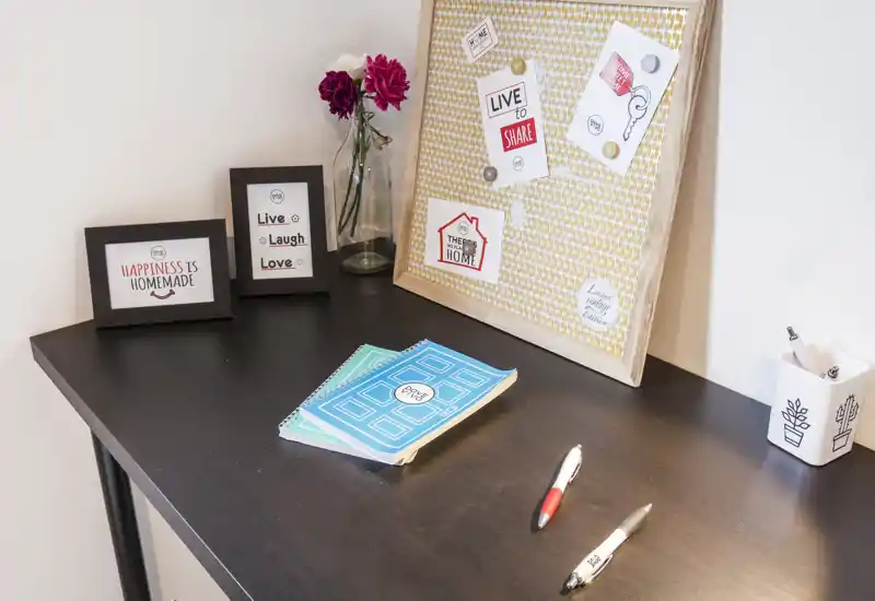 Un rincón de escritorio ordenado con marcos decorativos, un corcho y material de papelería: un espacio de trabajo luminoso y perfecto para teletrabajo o estudio.