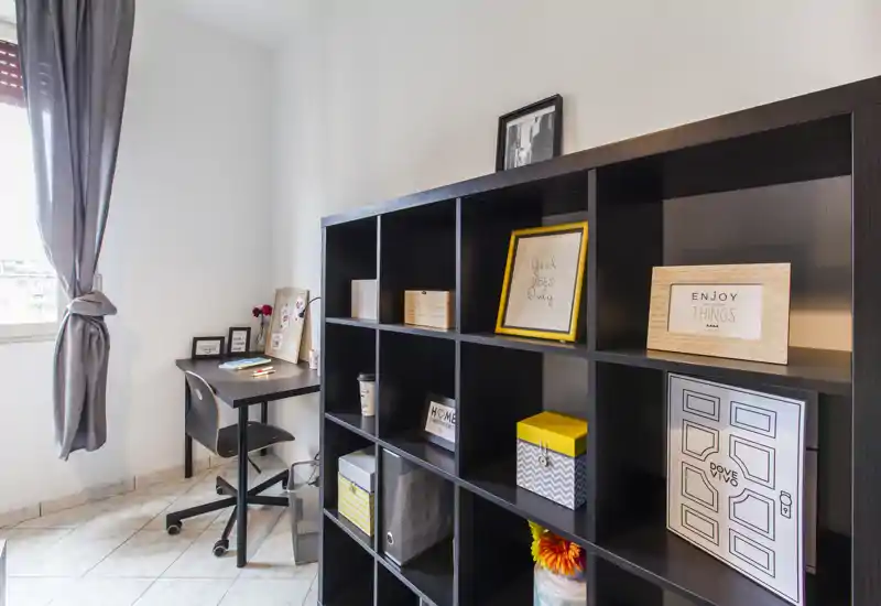 Zona de estar luminosa y moderna con una gran estantería de cubos y un pequeño escritorio junto a la ventana — ideal para un rincón de trabajo compacto o almacenamiento con estilo.