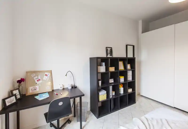 Rincón de dormitorio luminoso y moderno con escritorio, estantería modular y cama parcialmente visible; diseño limpio y zona de trabajo funcional.