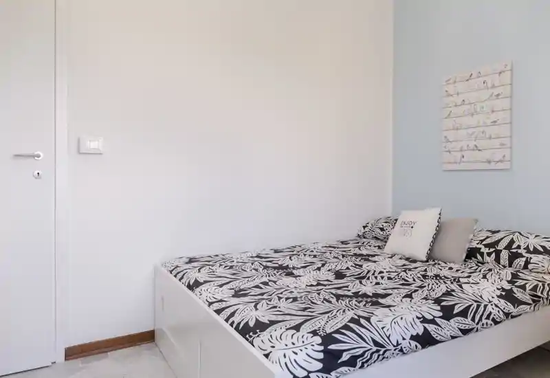 Dormitorio luminoso y moderno con edredón estampado, cojines decorativos y pared minimalista — ideal para una estancia acogedora de uno o dos huéspedes.