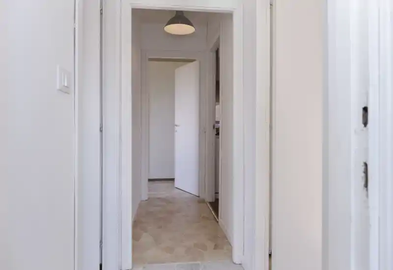 Un pasillo/entrada luminoso y neutro con suelo de baldosas y una puerta interior parcialmente abierta; un paso sencillo y bien iluminado ideal para mostrar el espacio de circulación.