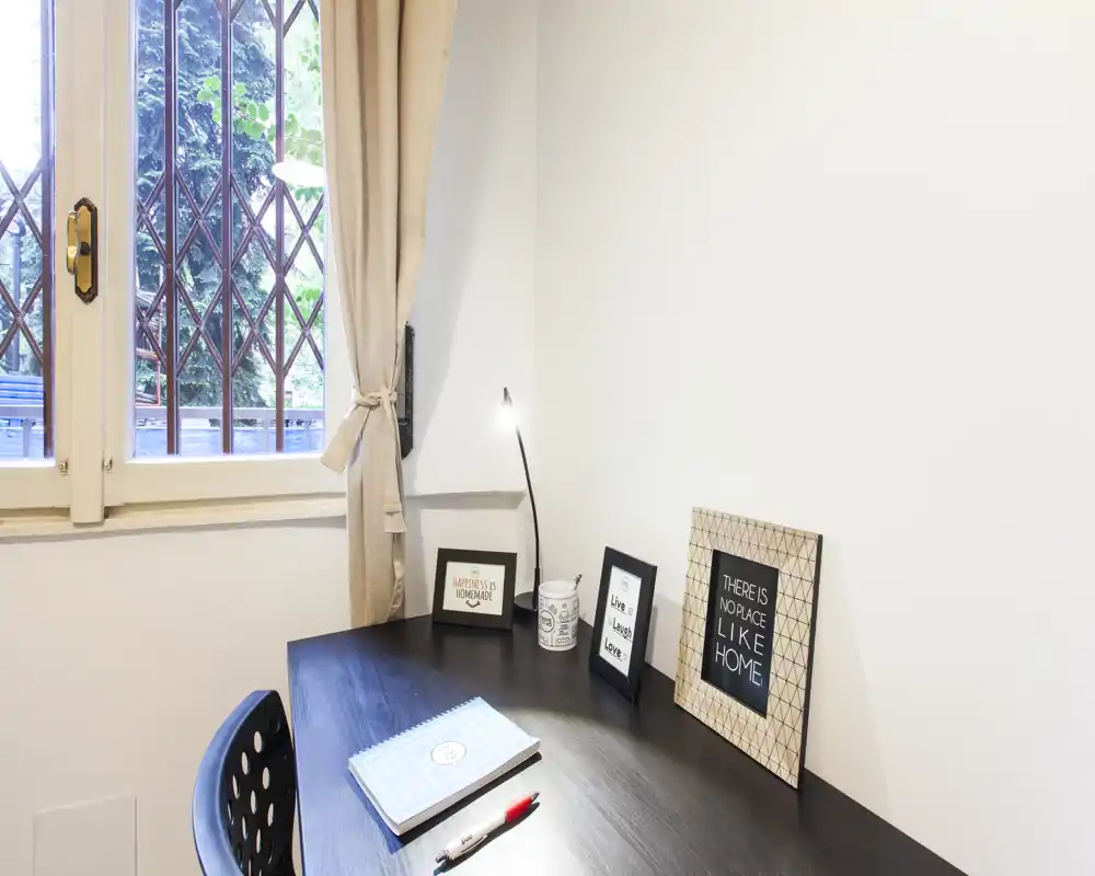 A compact, well-lit workspace by a window with a desk, lamp and decorative framed prints — ideal for studying or remote work.