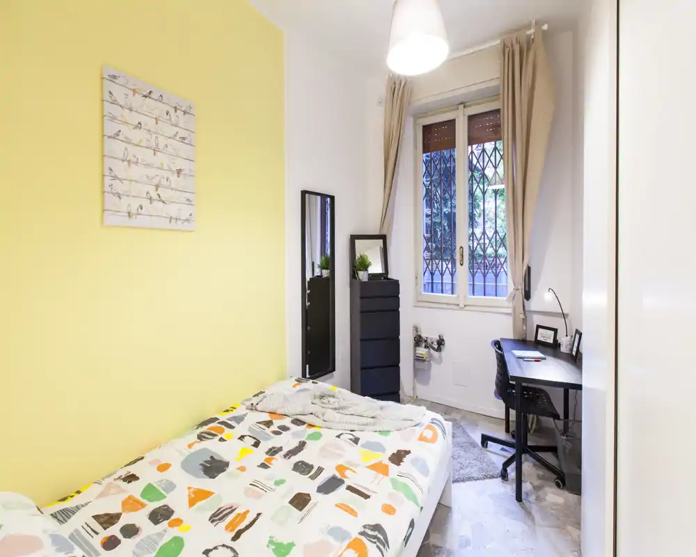 Bright, well-staged single bedroom with a patterned bedspread, bedside storage, a desk by the window and soft neutral curtains — ideal for a student or single occupant.