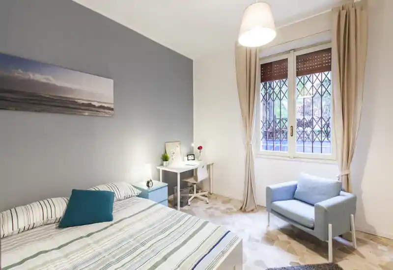 Bright, modern bedroom with a striped double bed, a small desk by the window and a comfortable armchair — ideal for relaxing or working.