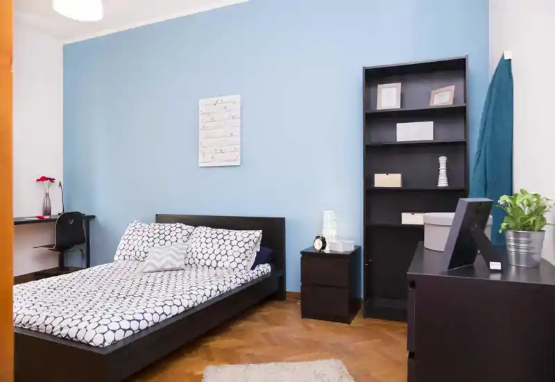 Bright, tidy bedroom with a double bed, patterned bedding, bedside table and shelving — modern, welcoming and well lit.