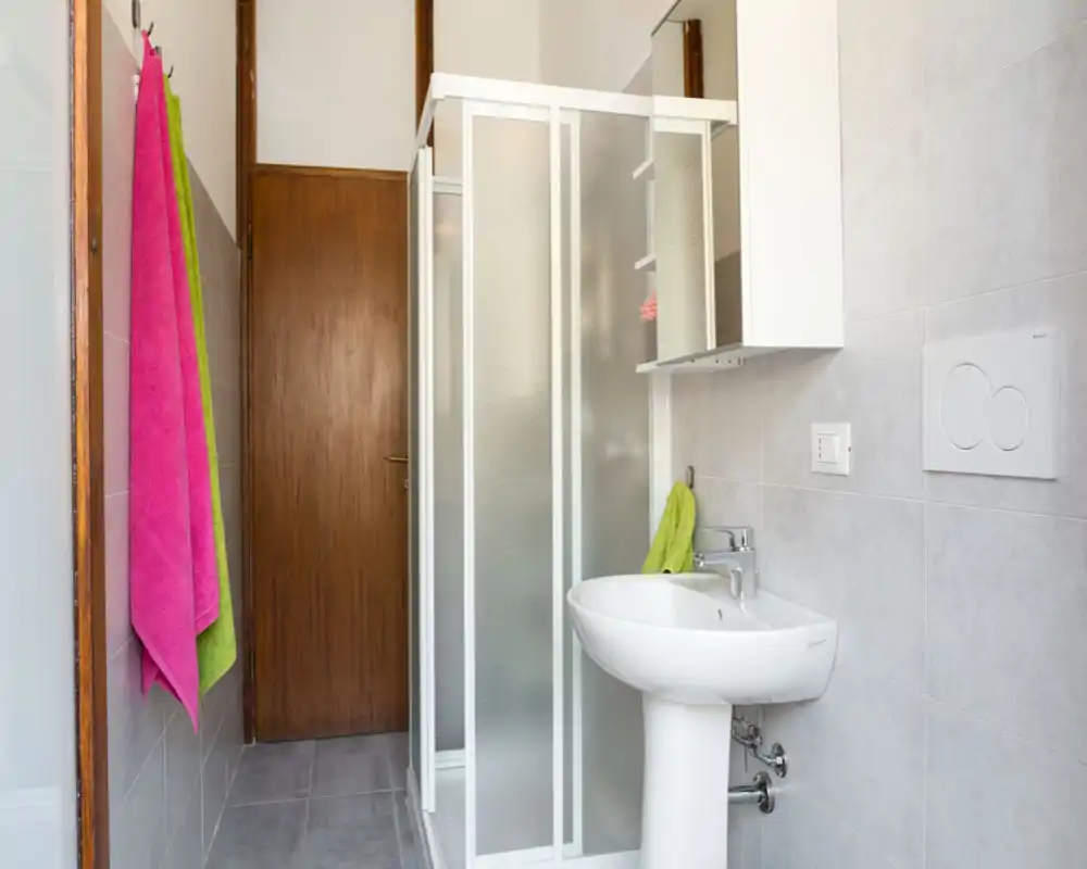 Baño moderno y limpio con lavabo de pie, ducha con cristal esmerilado y toallas de colores vivos.