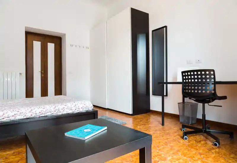 Dormitorio luminoso y de mobiliario sencillo con cama doble, armario y escritorio — ideal para alquileres de corta estancia. Suelo cálido con diseño y distribución minimalista.