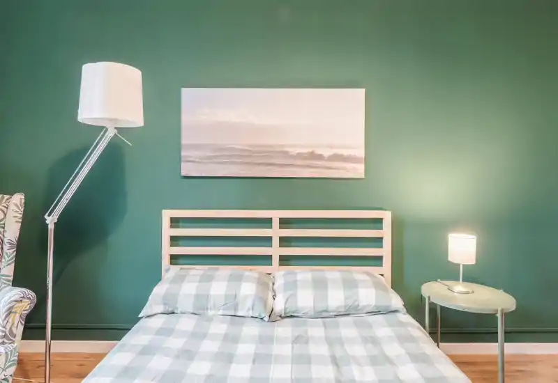 Dormitorio luminoso y cuidado con cabecero de listones de madera, ropa de cama a cuadros y luz ambiente suave — ideal para destacar una cama acogedora en el anuncio.