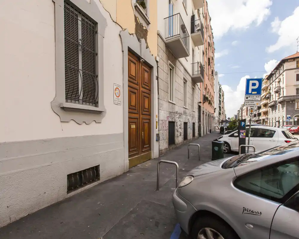 Vista de la calle con acera, coches aparcados y fachadas de edificios con buena luz diurna — adecuada para destacar la ubicación y el acceso por la calle.