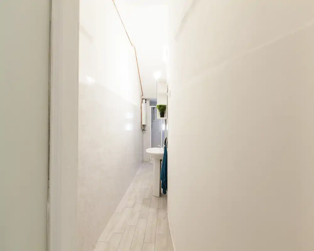 Baño estrecho con lavabo de pie, accesorios en pared y baldosas claras; limpio, luminoso y con buena nitidez — perfecto para anuncios de alojamientos compactos.