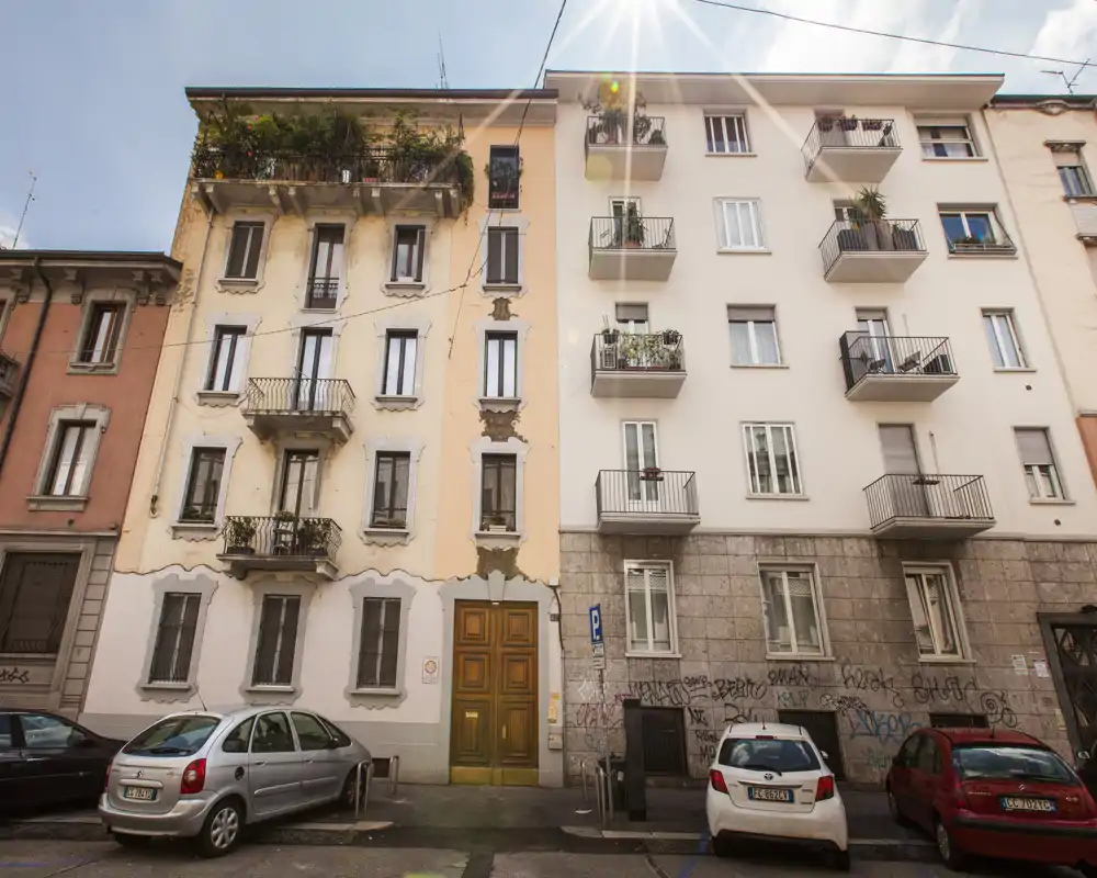 Foto exterior a la calle de un edificio de viviendas de varios pisos con pequeños balcones y coches aparcados, útil para mostrar la fachada y la ubicación.