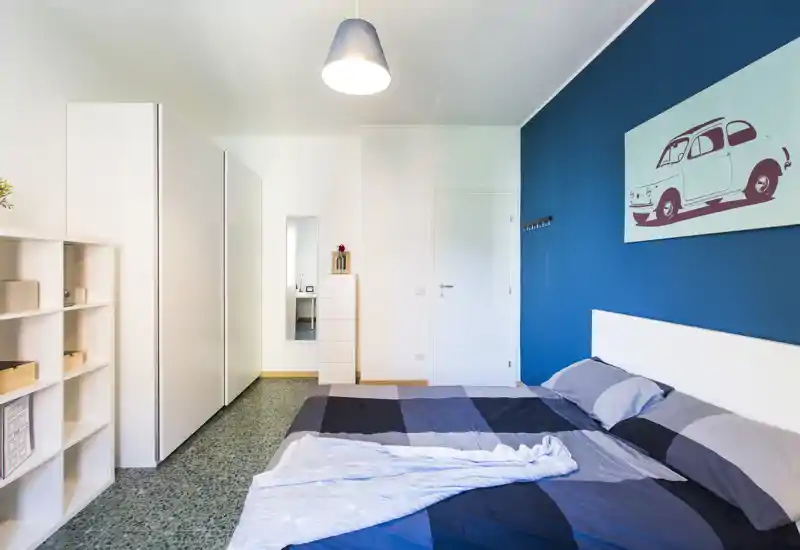 Bright, modern bedroom with a double bed, bold blue accent wall and minimalist white storage units creating a clean, stylish space.