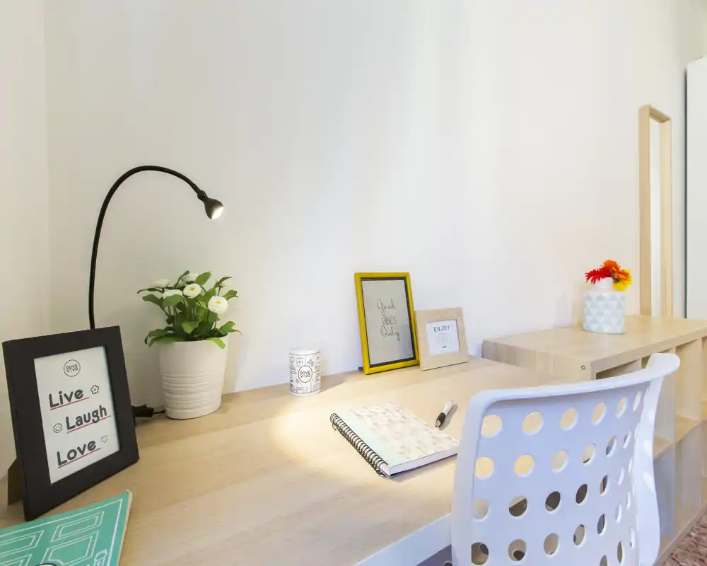 Angolo studio luminoso e minimale con sedia bianca forata, cornici decorative, una pianta in vaso e una lampada da scrivania — un angolo lavoro ordinato e ideale per concentrarsi.