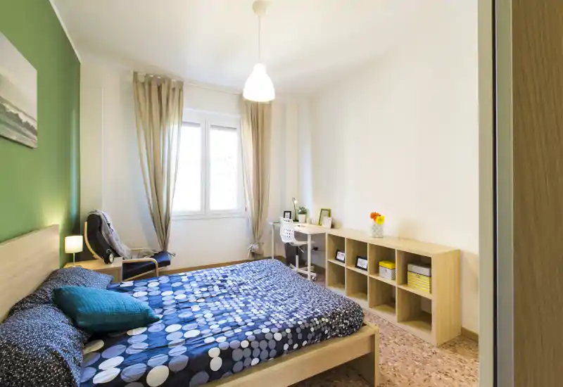 Camera da letto luminosa e ben arredata con letto matrimoniale, poltrona per la lettura vicino alla finestra e scrivania con scaffalatura: perfetta per affitti brevi che cercano comfort e funzionalità.