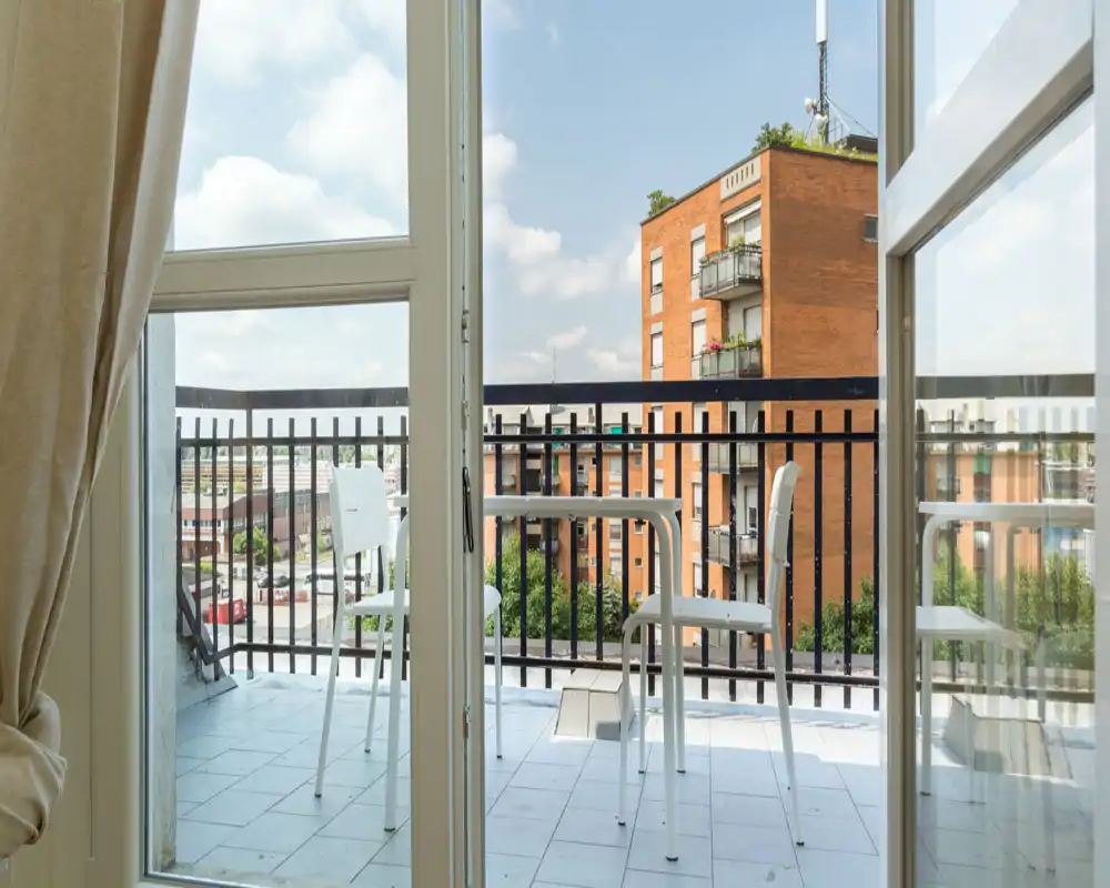 Balconcino soleggiato con piccolo tavolo e due sedie, vista sugli edifici vicini — ideale per il caffè del mattino.