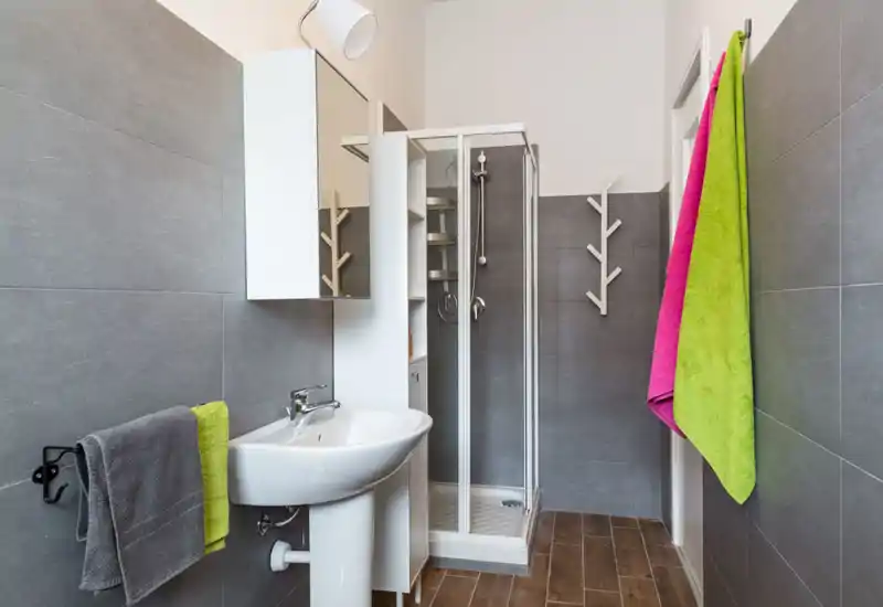 Bagno moderno e ben illuminato con box doccia angolare, lavabo a colonna, armadietto con specchio e asciugamani colorati che danno contrasto.