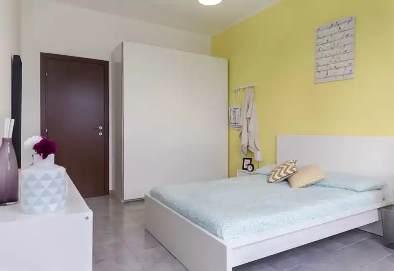 Bright, simply styled bedroom with a double bed, light bedding and a neutral décor; the bed is the primary focal point of the room.