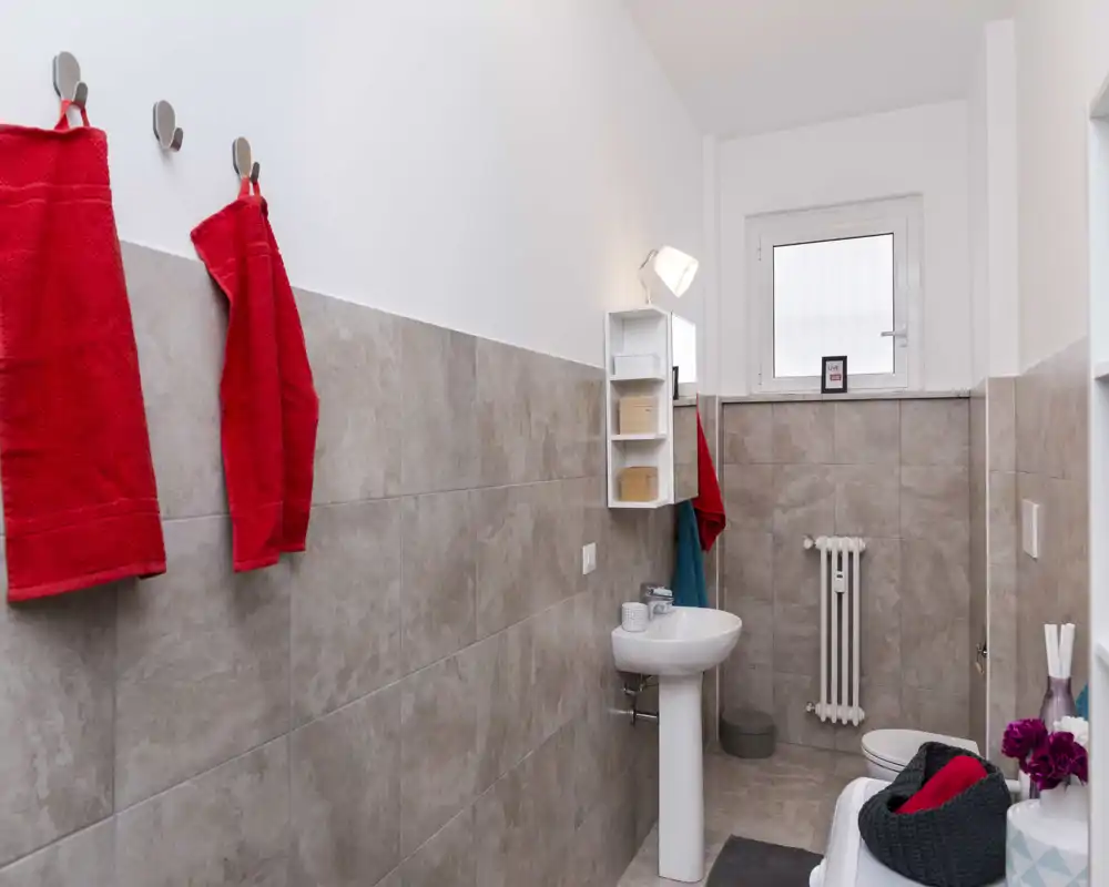 Piccolo bagno con lavabi a parete e appenditutto; piastrelle chiare e asciugamani colorati sono visibili nonostante la distorsione dell'immagine.