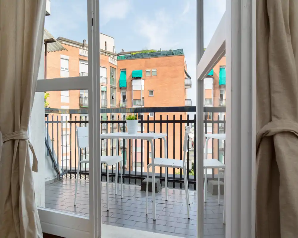 Sunny small balcony with a white table and chairs, shown through open glass doors; ideal for morning coffee with city views.