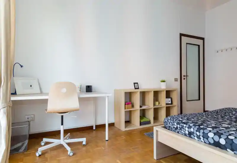 Bright, modern bedroom with a wooden platform bed, patterned duvet and a simple desk with chair by the window — minimal, tidy and well lit.