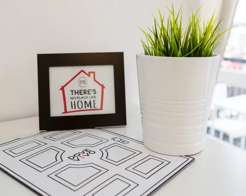 Gros plan d'une table décorative avec un pot blanc contenant une plante et un cadre portant "There's no place like home". Style lumineux et minimal, parfait pour un cliché d'ambiance.