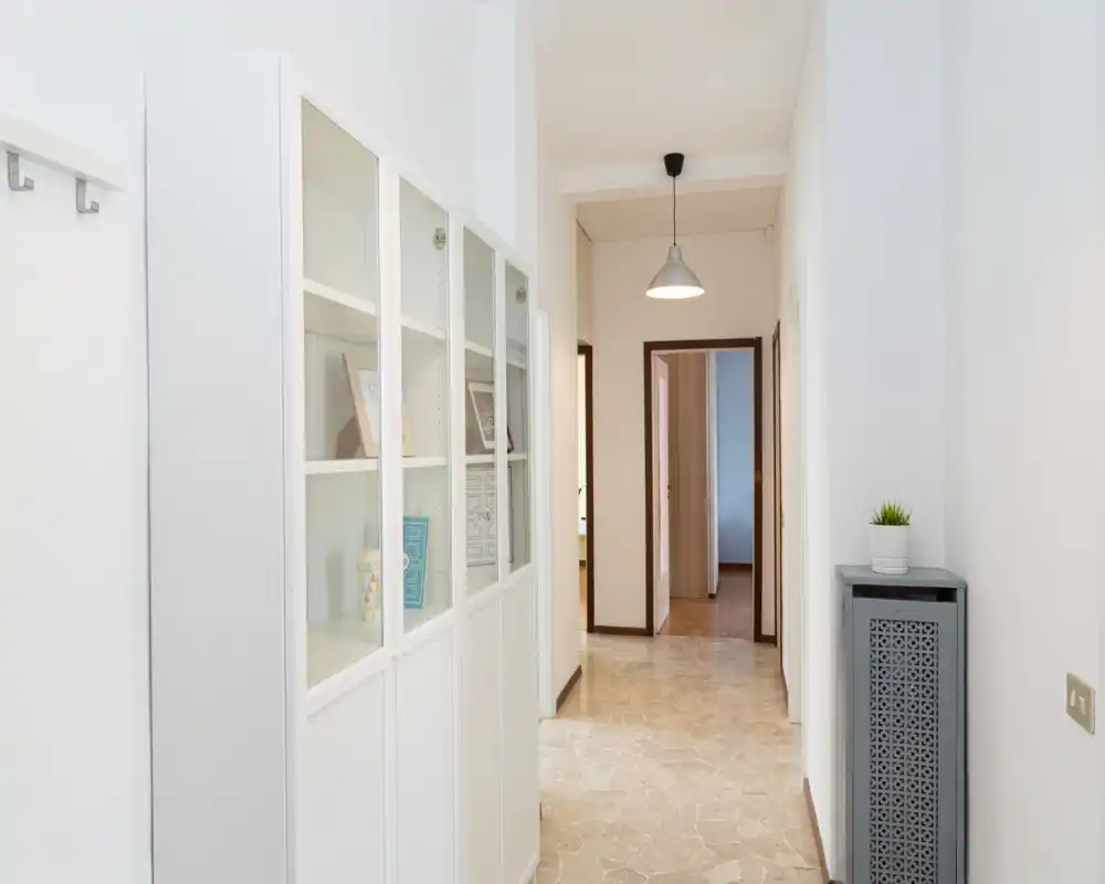 Bright, modern entrance hallway with white built-in storage cabinets, pendant light and tiled floor — ideal as an inviting corridor to the apartment.