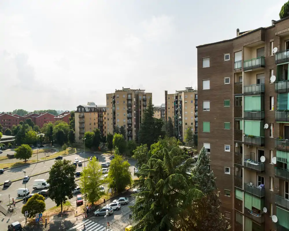 View from a balcony overlooking a residential street and neighboring apartment blocks with trees and parked cars; bright daytime scene ideal for showcasing location and surroundings.