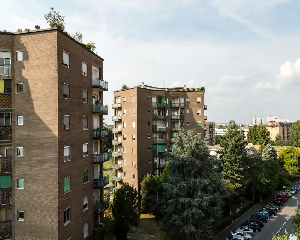 Exterior view of residential apartment buildings with balconies, trees and parked cars, offering a clear urban panorama and natural light.