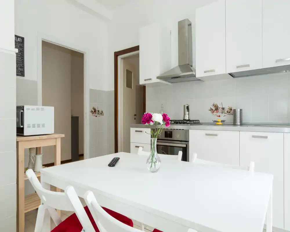 Bright, modern kitchen with white cabinets, a stainless-steel gas hob and oven, and a dining table with a vase of flowers creating a clean, welcoming space.