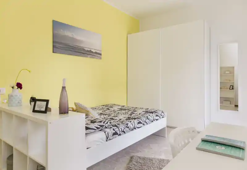 Dormitorio luminoso y bien decorado con cama doble, ropa de cama estampada, pared amarilla y amplio armario blanco — ideal para anuncios.