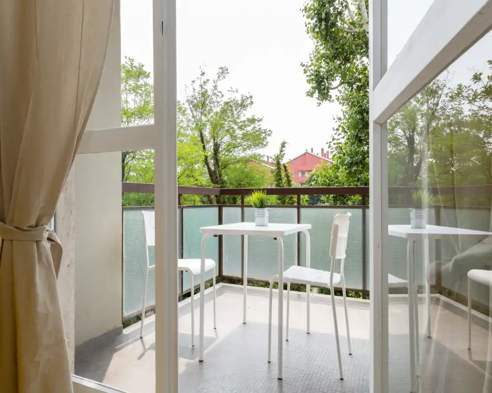Sunny private balcony with a small white table and two chairs, overlooking green trees — ideal for morning coffee or relaxing outdoors.