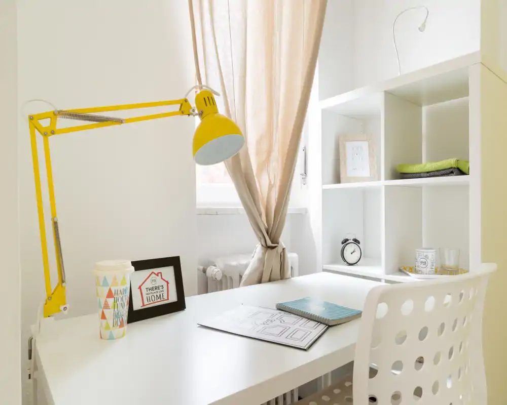 Bright, tidy home office corner with a white desk, yellow adjustable lamp and shelving — perfect for focused work or study.