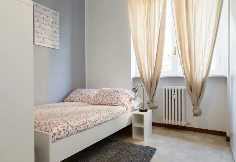 Dormitorio individual luminoso y ordenado con ropa de cama estampada, mesita y luz natural suave desde la ventana — ideal para un anuncio acogedor.