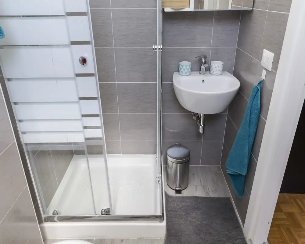 Bagno moderno e compatto con box doccia in vetro, lavabo sospeso e pareti piastrellate — luminoso, ordinato e funzionale per soggiorni brevi.