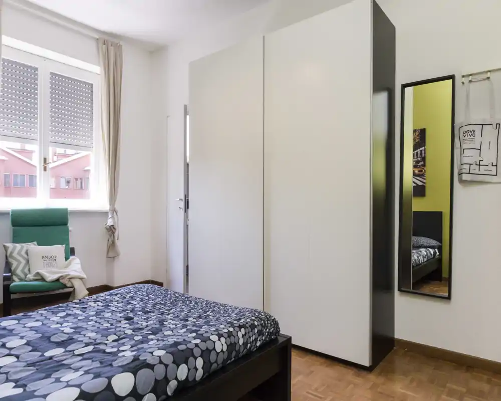 Camera da letto luminosa e ben arredata con letto matrimoniale, grande armadio e una poltrona accogliente vicino alla finestra.