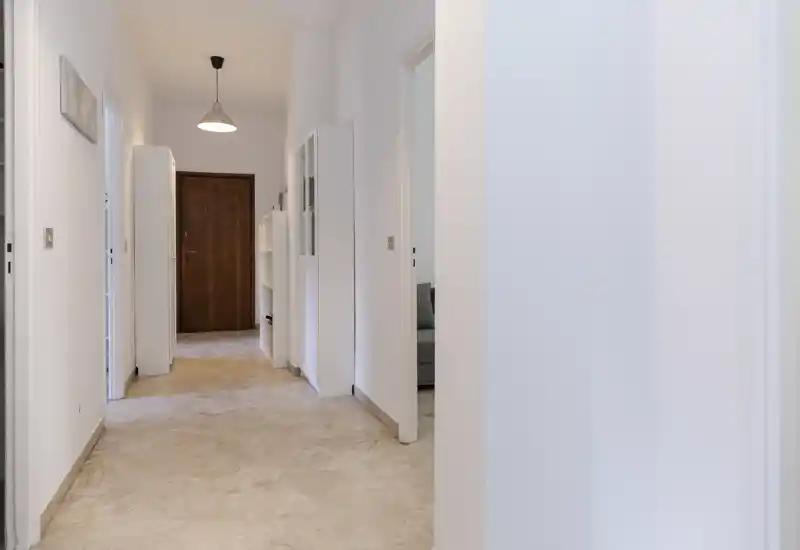 Vestíbulo luminoso y minimalista con suelo de baldosas que conduce a una puerta de entrada de madera, paredes blancas neutras y lámpara colgante sencilla — una entrada limpia y acogedora.