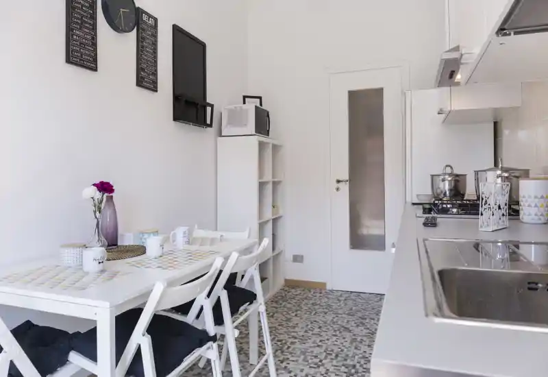 Cocina luminosa y compacta con rincón comedor integrado: mobiliario blanco, vitrocerámica a gas y una pequeña mesa para cuatro crean un espacio funcional y acogedor, perfecto para apartamentos urbanos.