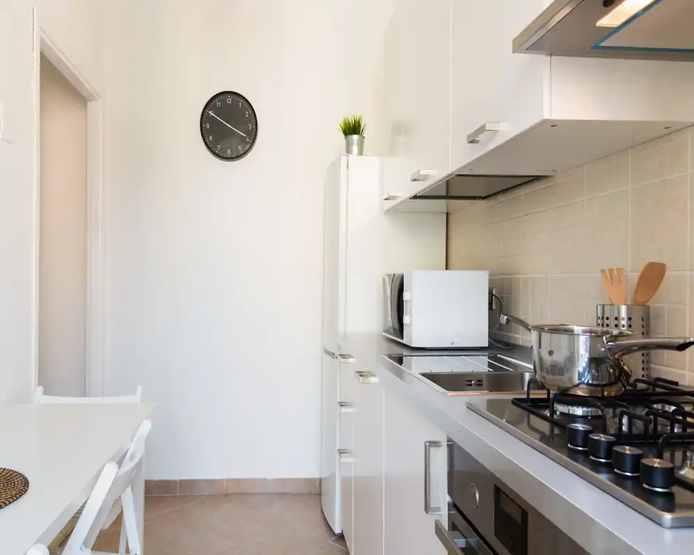 Cucina moderna e luminosa con piano cottura a gas, forno a microonde e piccolo angolo pranzo — spazio compatto, pulito e ideale per soggiorni brevi.