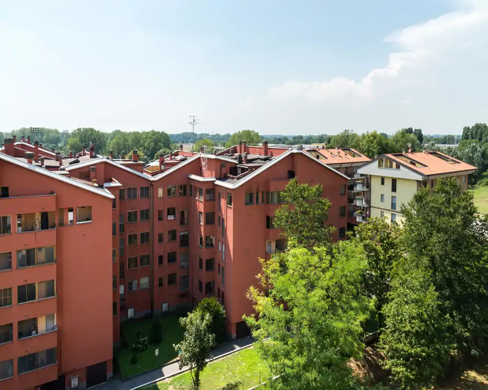Vista esterna di edifici residenziali con facciate rosse e alberi verdi sotto la luce del giorno — ideale per mostrare lo stabile e l'area verde circostante.