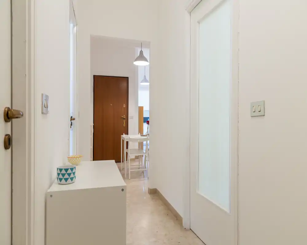 Ingresso luminoso e minimale con una consolle bianca e vista verso la porta d'ingresso e la zona pranzo — linee pulite e toni neutri per un'accogliente prima impressione.
