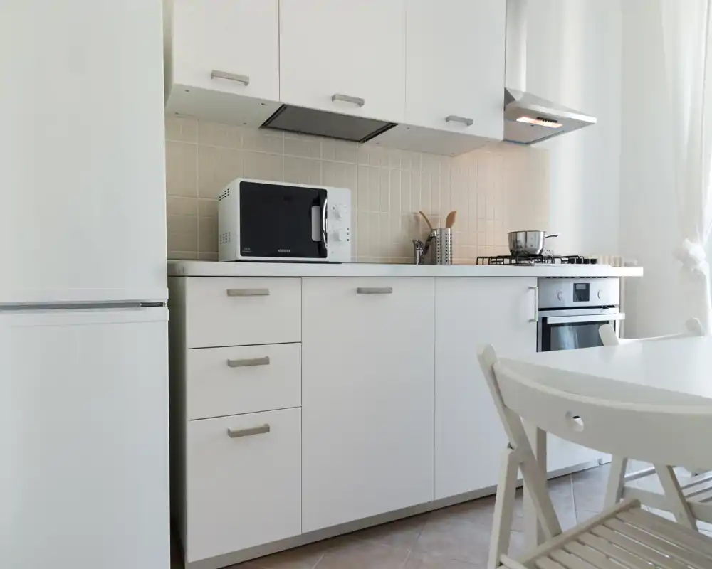 Cucina moderna e luminosa con mobili bianchi, piccoli elettrodomestici e un tavolo da pranzo: pulita, minimale e ben illuminata per foto annuncio.