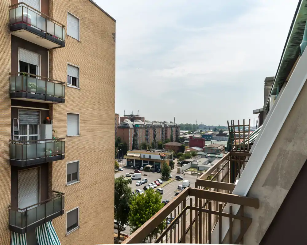 Balcone soleggiato dell’appartamento con vista su edifici vicini, parcheggi e il panorama urbano in lontananza — ottimo per mostrare uno spazio esterno cittadino.