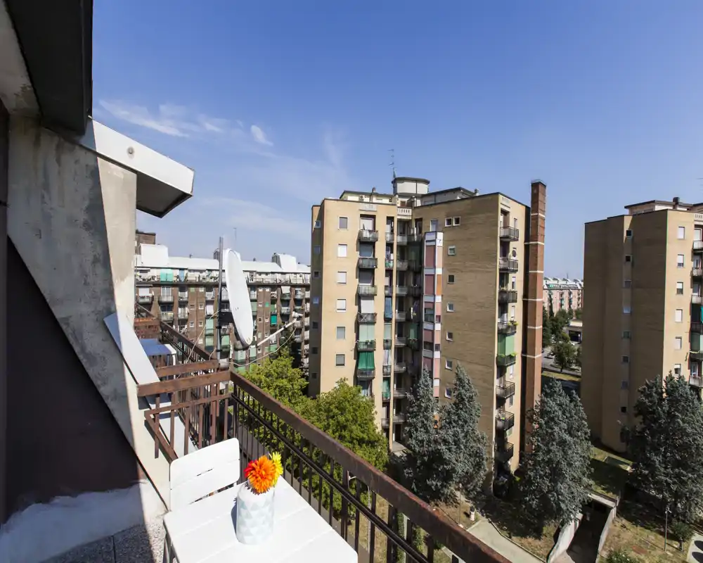 Balcón privado soleado con una pequeña mesa blanca y vistas a edificios residenciales y copas de árboles — ideal para el café matutino y relajarse en la ciudad.