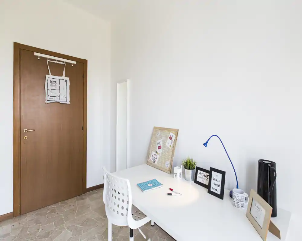 Rincón de oficina en casa compacto con escritorio blanco, lámpara de trabajo, marcos decorativos y una pequeña planta: luminoso, minimalista y listo para trabajar.