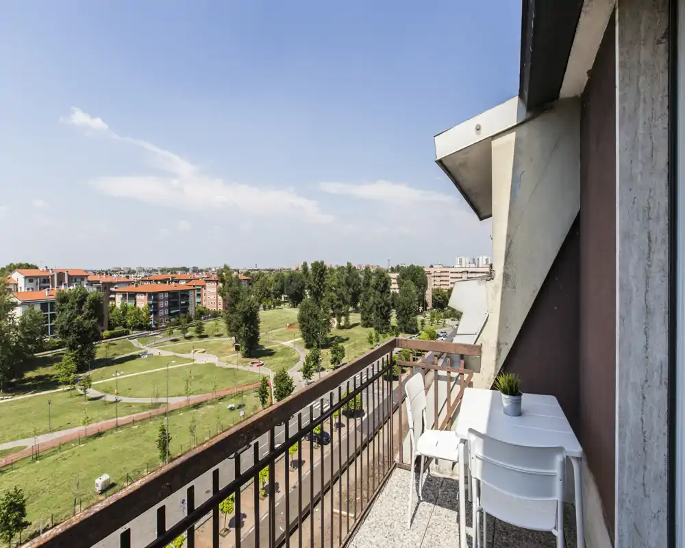Balcón soleado con mesa y sillas que da a un parque verde y tejados residenciales — ideal para un café matutino y relajarse al aire libre.