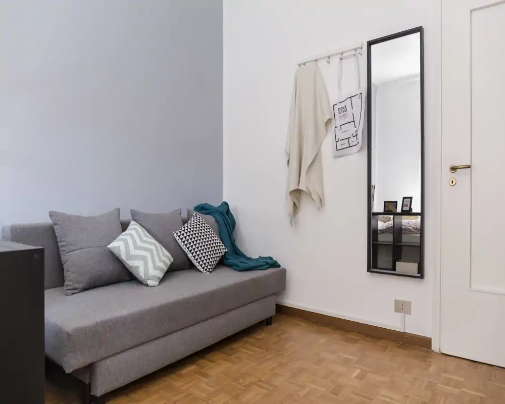 Espace de vie lumineux et moderne avec canapé gris, coussins à motifs et miroir mural — pièce soignée et accueillante pour se détendre.