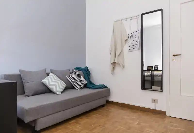 Zona giorno luminosa e moderna con divano grigio, cuscini decorativi e specchio a parete — ambiente ordinato e accogliente ideale per il relax.