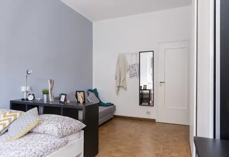 Chambre lumineuse et soignée avec linge de lit à motifs, coussins et tête de lit étagère ; tons neutres et parquet en bois pour une ambiance chaleureuse et contemporaine.