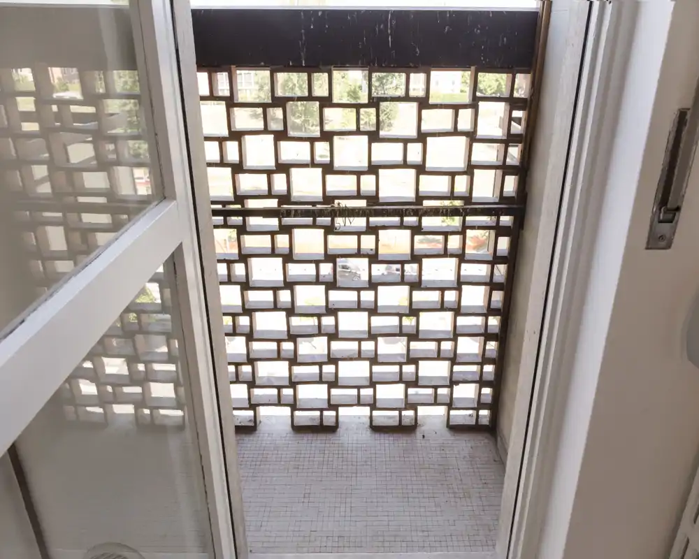 Petit balcon extérieur avec une paroi en briques ajourées offrant intimité et vue partielle. Sol carrelé et porte-fenêtre coulissante reliant l'intérieur à cet espace extérieur compact.