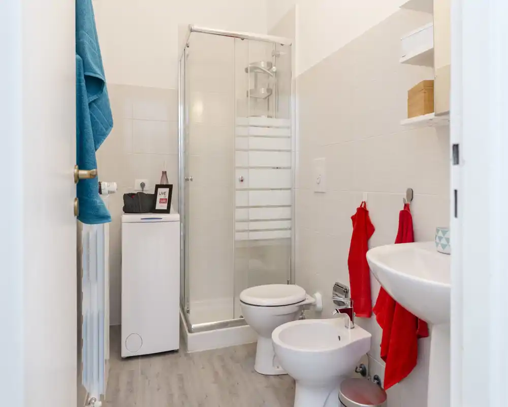 Salle de bains compacte et moderne avec cabine de douche en verre, WC, bidet et lavabo. Carrelage neutre et éclairage lumineux pour un espace propre et fonctionnel.
